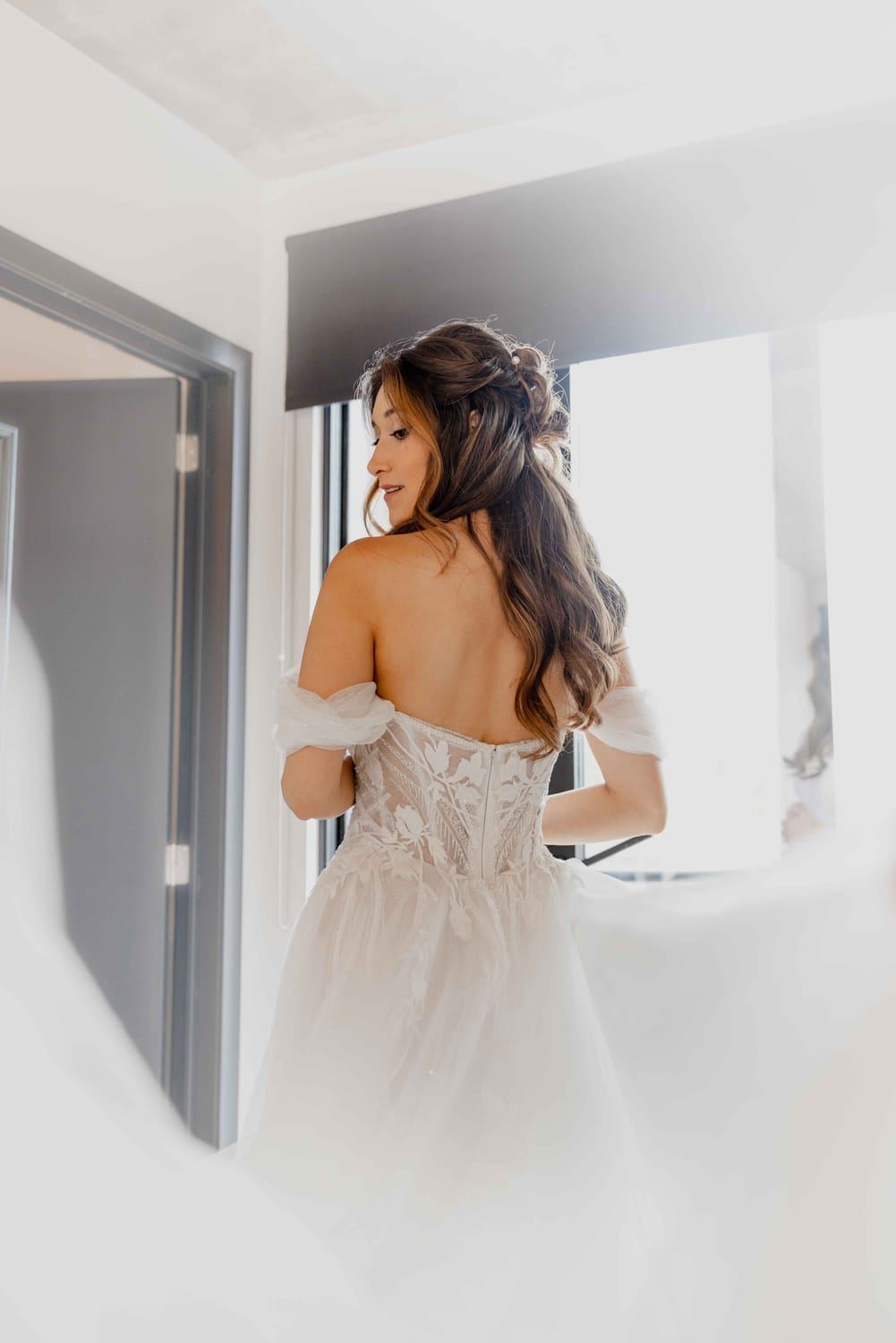 Bride in a lace dress by the window, seen from behind