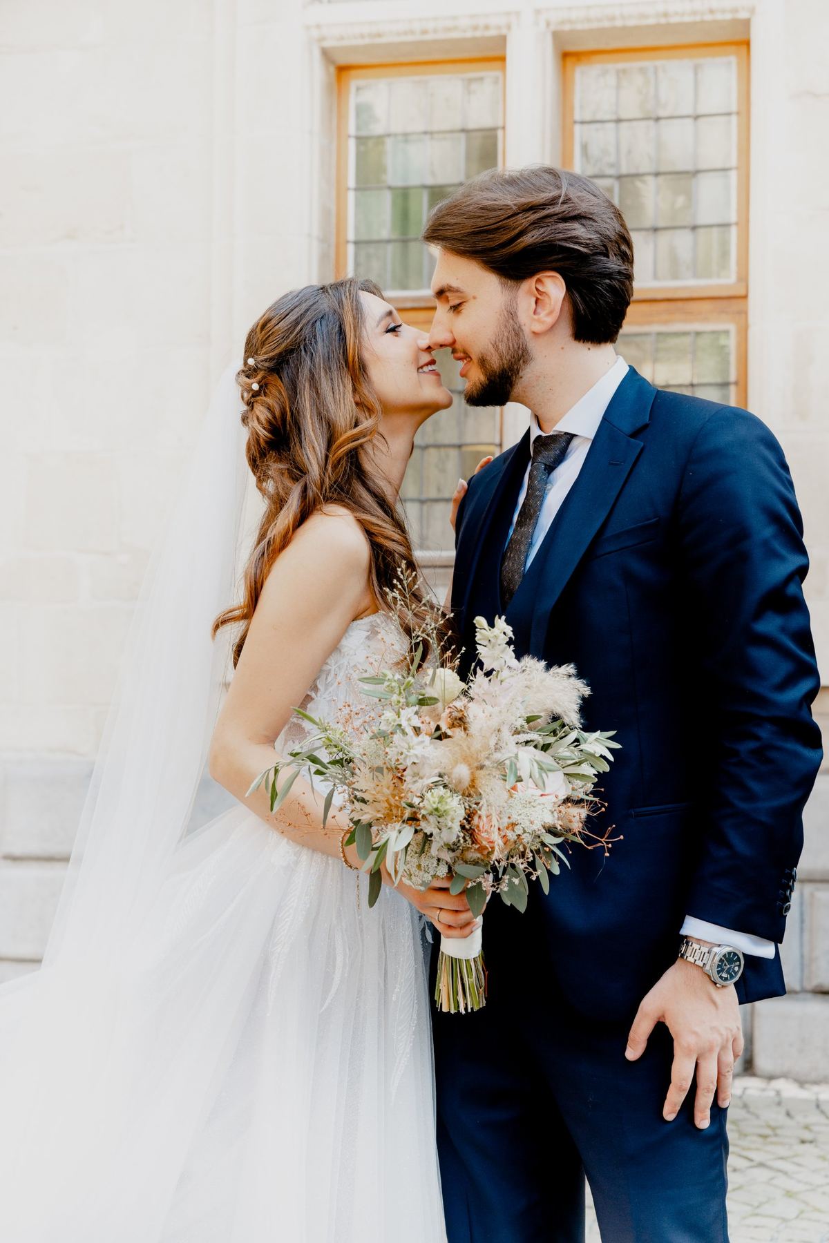Bride and groom nose to nose, she holds a dried-flower bouquet