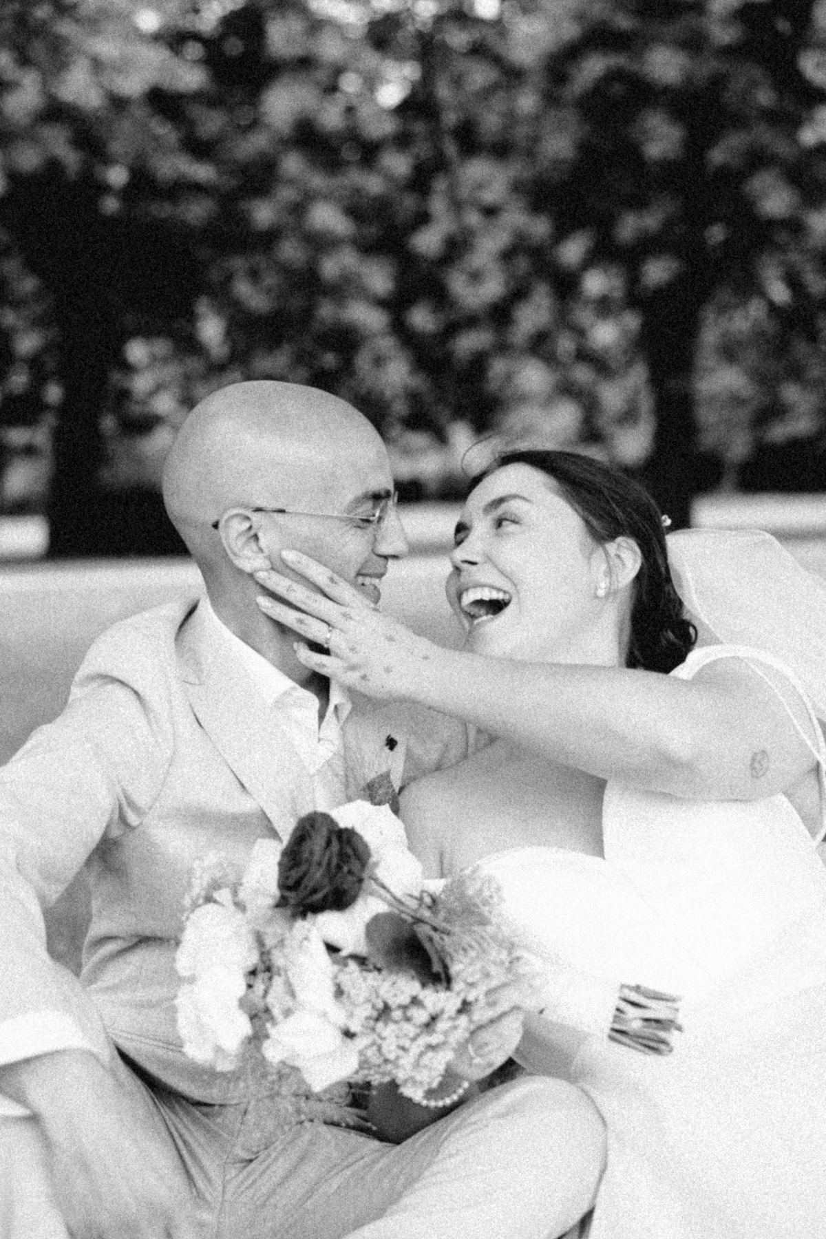 Bride laughing with her hand on the groom’s face, in black and white