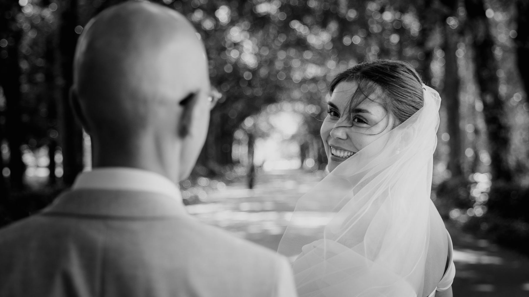 Bride smiling back over her shoulder at the groom, in black and white