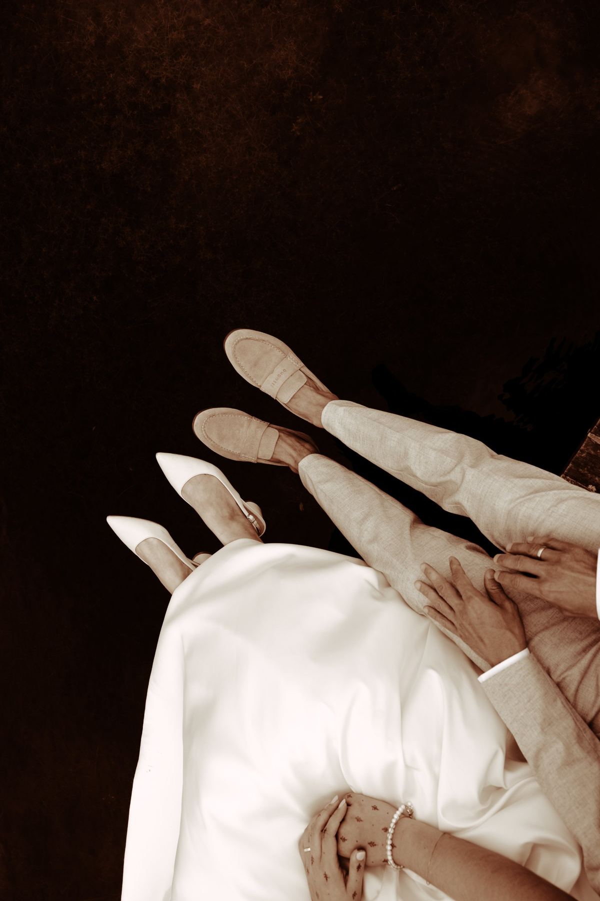 Seen from above: the couple’s shoes and hands, in warm sepia